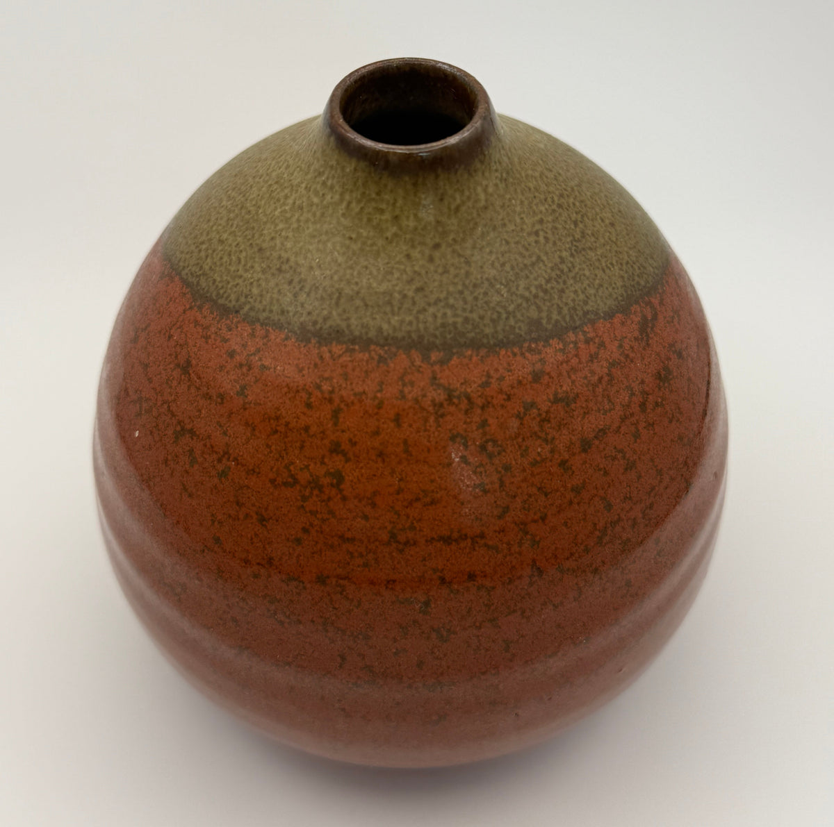 A handmade ceramic vase with a rounded, bulbous shape and a short, narrow neck, featuring a two-tone glaze. The top section has a speckled brown, while the larger bottom section has a textured terracotta-brown glaze with dark speckles.