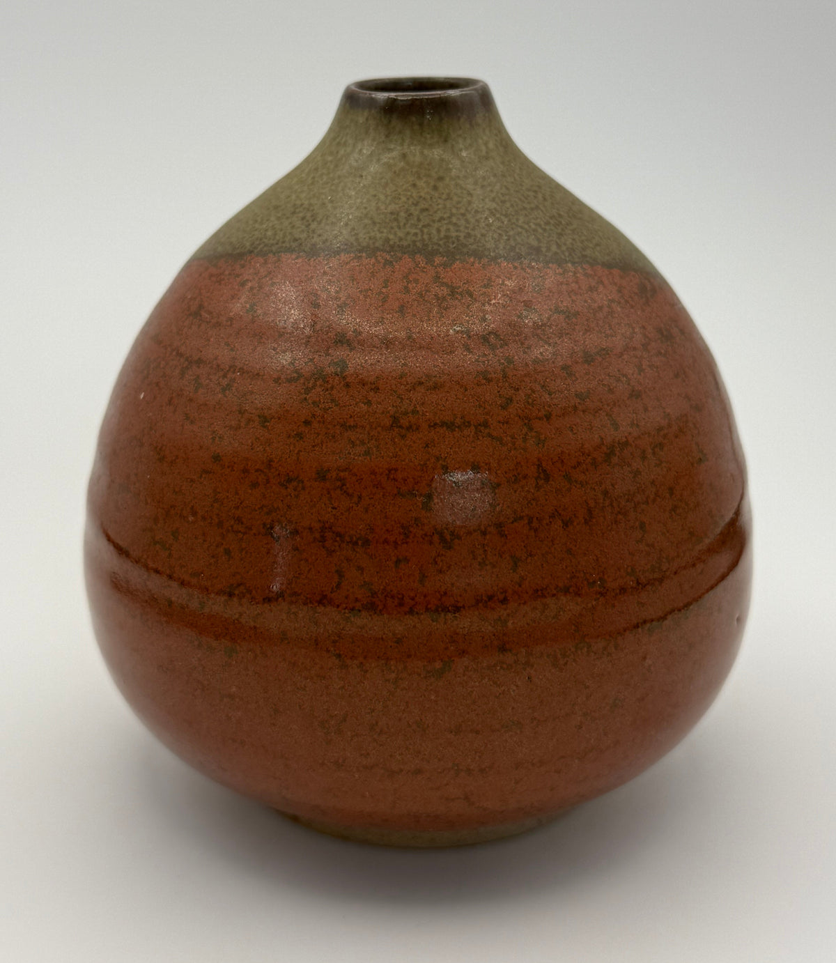 A handmade ceramic vase with a rounded body, a narrow neck, and a small top opening. It features a glossy reddish-brown glaze with dark speckles on the lower portion and a matte brown glazed section on the upper portion, set against a white background.